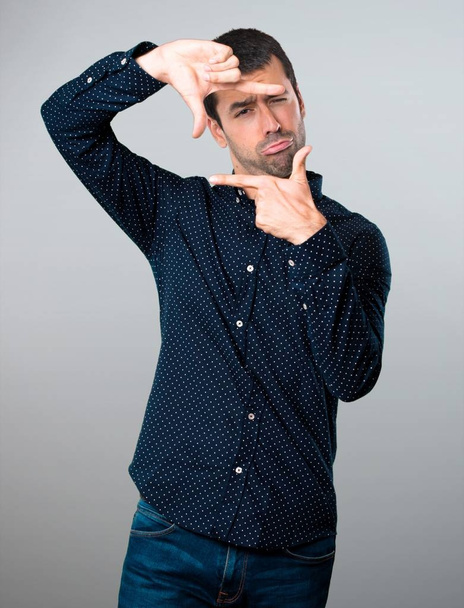 Hombre guapo enfocándose con los dedos sobre fondo gris
 - Foto, Imagen