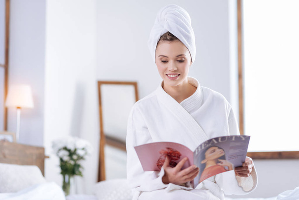 Pretty woman in bathrobe reading magazine in bedroom - Фото, зображення