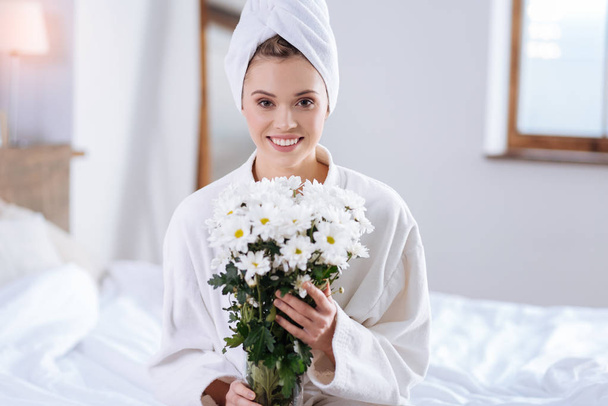 Happy woman in bathrobe holding bouquet of flowers - 写真・画像