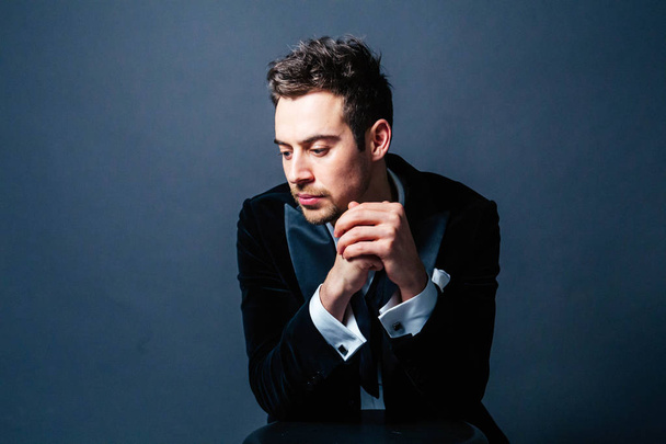 Portrait of a young handsome man in a suit, upset, hands together, looking down, against plain studio background - Photo, Image