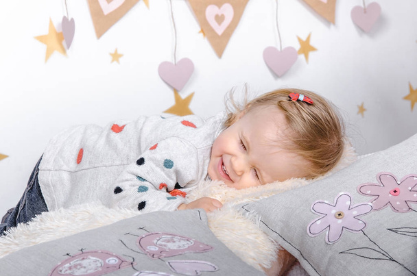 Κοντινό πλάνο λίγο χαμογελαστό κορίτσι μωρό στο φόντο του δωματίου ενός παιδιού. Ημέρα του Αγίου Βαλεντίνου διακόσμηση εσωτερικών. - Φωτογραφία, εικόνα