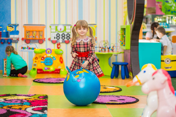 Happy smiling little girl jumping on a big rubber ball. Funny child having fun in play room - Foto, imagen
