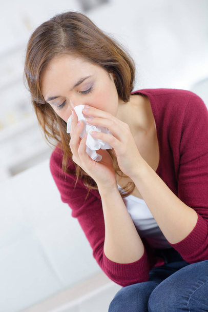 ill young woman is sneezing in a tissue - Photo, image