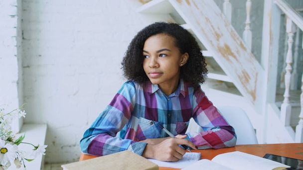Teenage curly haired mixed race young girl sitting at the table concentrating focused learning lessons for examination to univercity - 写真・画像