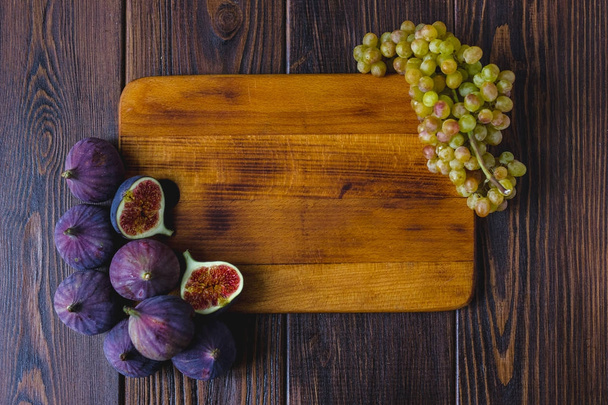 Wooden kitchen board with fig fruits and grapes on it. - Фото, зображення