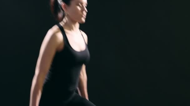 Slender woman does forward lunges while keeping dumbbells in her hands in a studio                      A wonderful view of a sportive woman in a black suit who does forward lunges while keeping metallic dumbbells in her hands in a black studio  - Metraje, vídeo