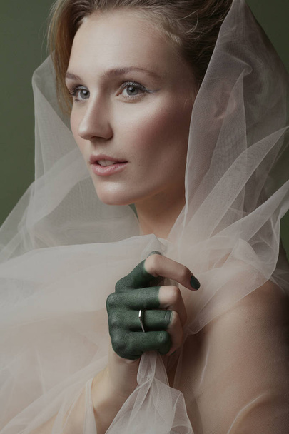 Beautiful girl with creative make-up and silvery jewelry on a green background - Фото, изображение