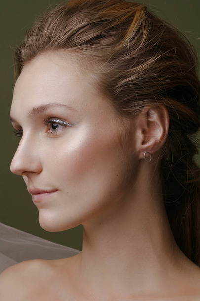 Красивая девушка с творческим макияжем и серебристыми украшениями на зеленом фоне
 - Фото, изображение