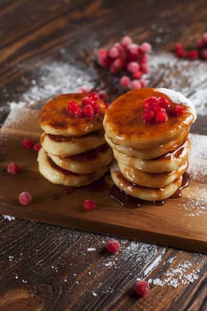 syrups with powdered sugar on a wooden cutting board, a sieve of a viburnum berry and caramel topping on a dark wooden table - Fotoğraf, Görsel