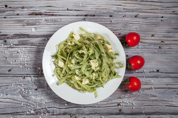 Спагетти со шпинатом зеленый с моцареллой, травы и помидоры на белой тарелке на светлом деревянном столе
 - Фото, изображение