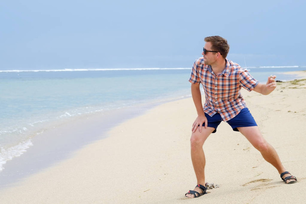 Happy caucasian man playing on beach throwing stones on ocean, Bali - Photo, Image