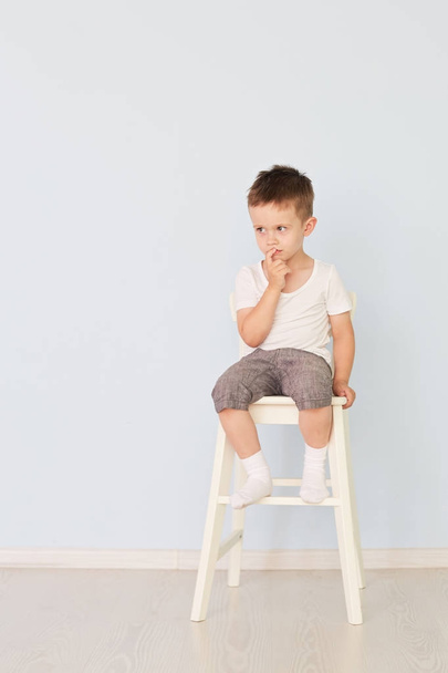 bright room. Boy in white shirt sitting in a high chair - Фото, изображение