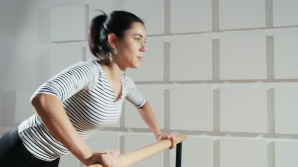 Sportive woman does push-ups on a wooden crossbar actively in a gym                                      An impressive view of a slender woman with a pony tail who does push-ups from a wooden crossbar installed in a gym. She does it energetically - Footage, Video