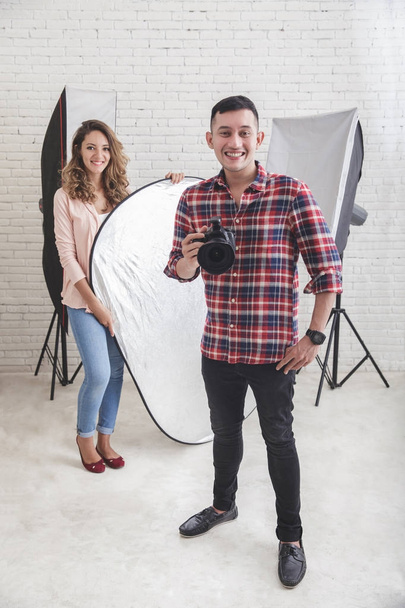 young photographer with his beautiful assistant in studio - 写真・画像