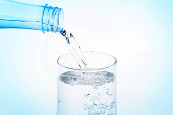 заливка води з пляшки в склянку на білому фоні
. - Фото, зображення