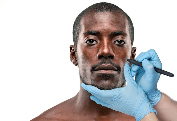 Surgeon drawing marks on male face against gray background. Plastic surgery concept - Photo, Image