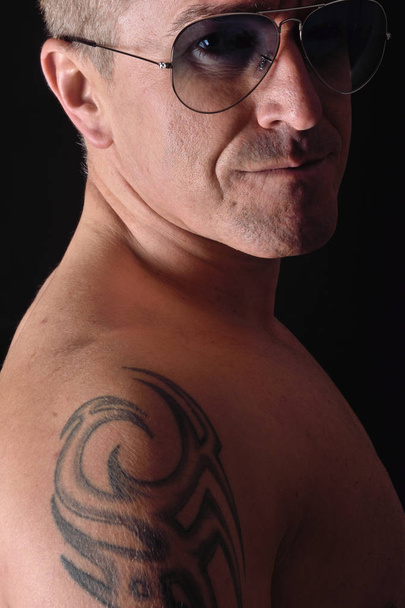 retrato de un hombre con tatuaje y gafas de sol y fondo negro
 - Foto, Imagen