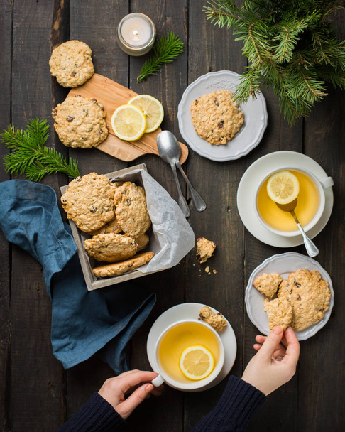 Το τέλειο γευστικό πρωινό. Oatmeal μπισκότα με σοκολάτα σε ξύλινο κουτί και πράσινο τσάι με λεμόνι σε κούπες σε σκούρο φόντο με ένα χριστουγεννιάτικο δέντρο. Καλύτερη χρήσιμοι Cookies. Επίπεδη lay, κορυφαία προβολή - Φωτογραφία, εικόνα