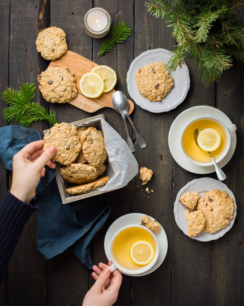 Το τέλειο γευστικό πρωινό. Oatmeal μπισκότα με σοκολάτα σε ξύλινο κουτί και πράσινο τσάι με λεμόνι σε κούπες σε σκούρο φόντο με ένα χριστουγεννιάτικο δέντρο. Καλύτερη χρήσιμοι Cookies. Επίπεδη lay, κορυφαία προβολή - Φωτογραφία, εικόνα