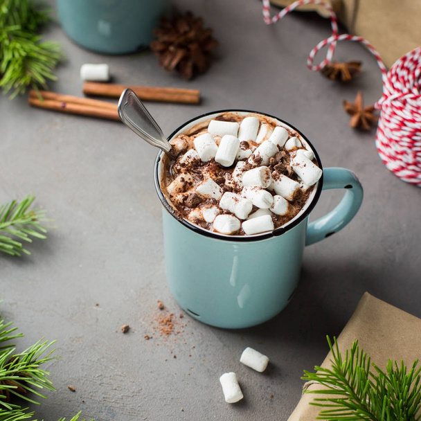 Mug of hot chocolate with marshmallow and cinnamon on a gray concrete background with a Christmas tree, gifts. and red-white string (twine). Winter xmas holidays concept. Festive mood. - Photo, image