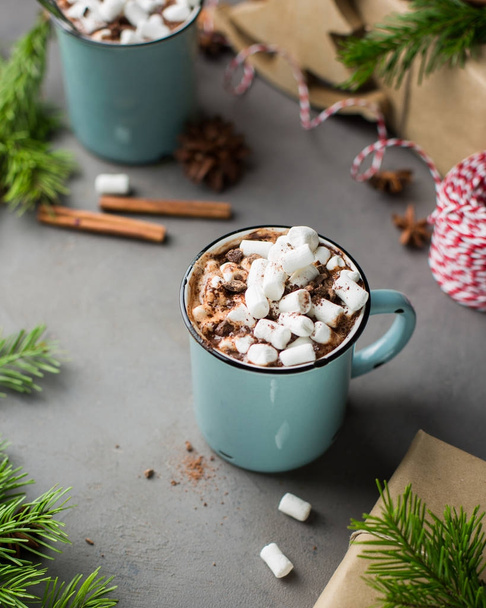 Mug of hot chocolate with marshmallow and cinnamon on a gray concrete background with a Christmas tree, gifts. and red-white string (twine). Winter xmas holidays concept. Festive mood. - Photo, Image