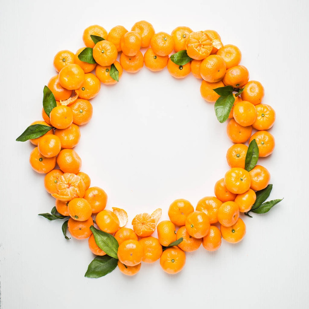 Christmas  tangerine mood!) Wreath made of  fresh small tangerines and green leaves on white wooden background. The best xmas celebration background.  Flat lay, top view, copy space.  - Foto, Bild