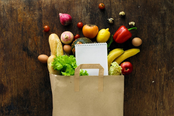 Paper bag of different health food and notebook on wooden background. Top view. Flat lay - Valokuva, kuva