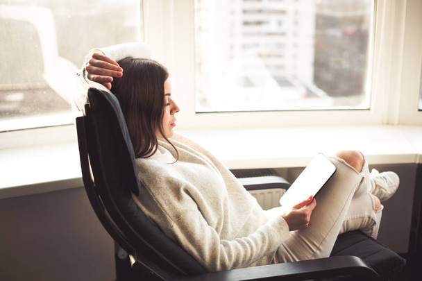 Frau sitzt mit E-Book am Fenster - Foto, Bild