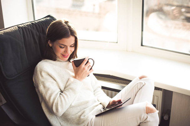 Mulher sentada junto à janela com um e-book
 - Foto, Imagem