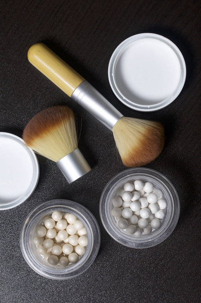 Golden and pearl highlighter in the form of balls in an open jar. Several cosmetic brushes lie side by side on the table. On a dark background, view from above. - Foto, immagini