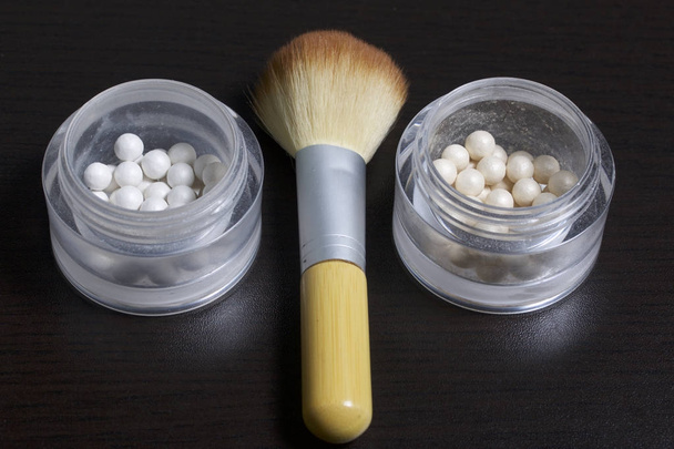 Golden and pearl highlighter in the form of balls in an open jar. Close to the brush for applying cosmetics. On a dark background, view from above. - Fotó, kép