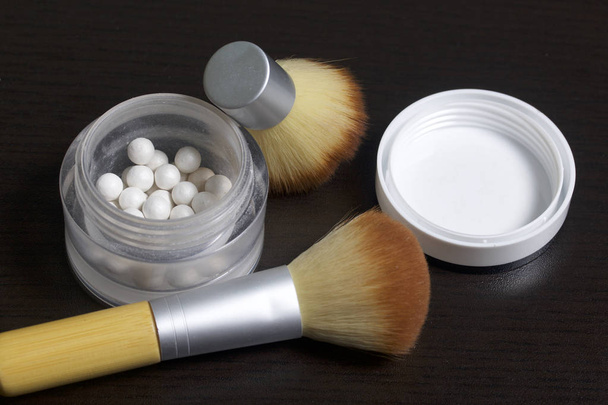 Pearl highlighter in the form of balls in an open jar. Close to the brush for applying cosmetics. On a dark background, view from above. - Fotó, kép
