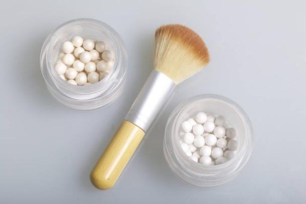 Golden and pearl highlighter in the form of balls in an open jar. Next to it is a cosmetic brush for applying it. On a dark background, view from above. - Фото, зображення