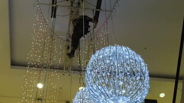 Промышленный альпинист устанавливает рождественские украшения в неподдерживаемом пространстве в торговом центре
 - Кадры, видео