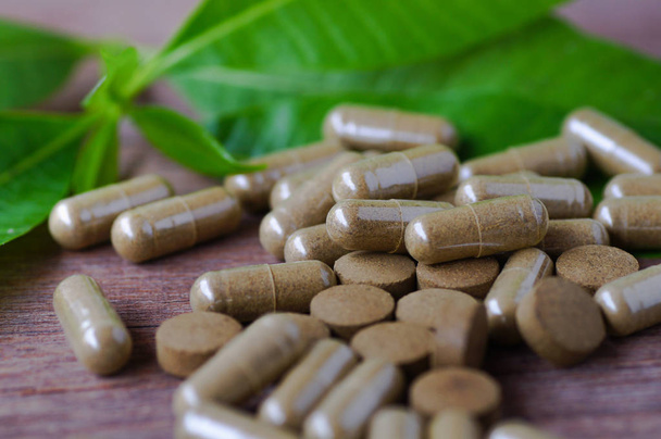 φυτικού φαρμάκου σε χάπι και κάψουλα σε ξύλινο τραπέζι με πράσινα φύλλα  - Φωτογραφία, εικόνα