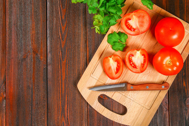 Fresh red tomatoes and sliced halves with cilantro on a wooden table. Top view. - Fotografie, Obrázek