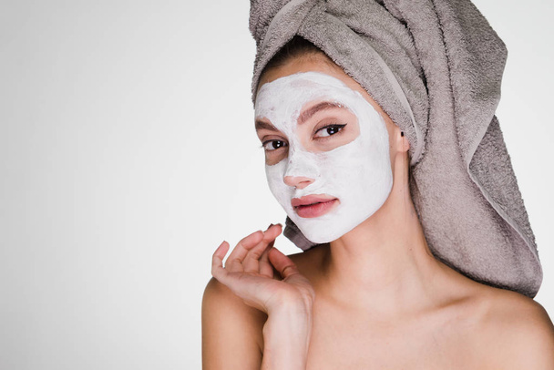 an attractive girl with a towel on her head wants clean skin on her face, has applied a white nutritious mask - Фото, изображение