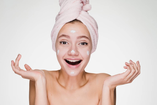 surprised happy girl with a towel on her head puts on the face nourishing cream - Photo, image
