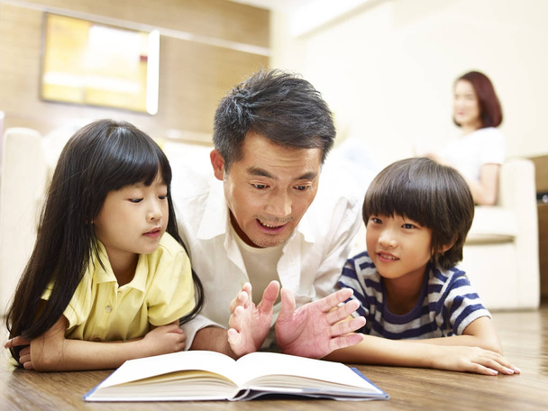 Aasialainen isä lukeminen kirja kertoo tarinan kaksi lasta
 - Valokuva, kuva
