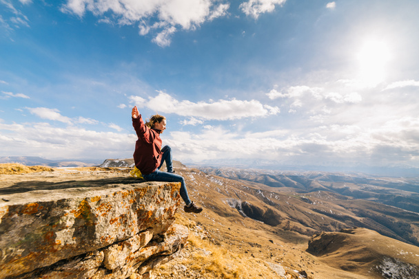 active young girl leads a healthy lifestyle, sits on the edge of the mountain and enjoys the sun and nature - Foto, imagen