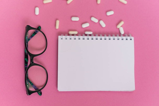 on a pink surface is a white notebook, pills and glasses - Foto, Bild
