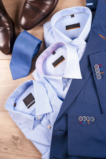 zestaw klasycznych męskich ubrań - niebieski garnitur, koszule, brązowe buty, pasek i krawat na drewnianym tle. - Zdjęcie, obraz