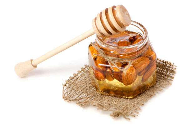 Een pot honing met een lepel voor honing noten amandelen - Foto, afbeelding