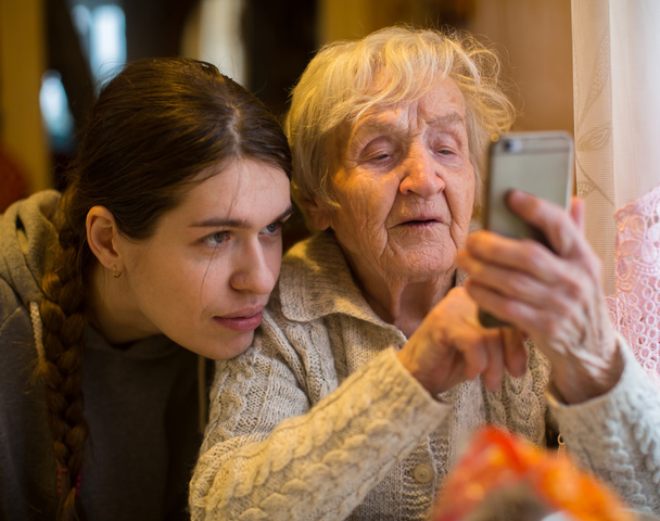 スマート フォンでアダルトの孫娘と高齢者の女性に見える - 写真・画像