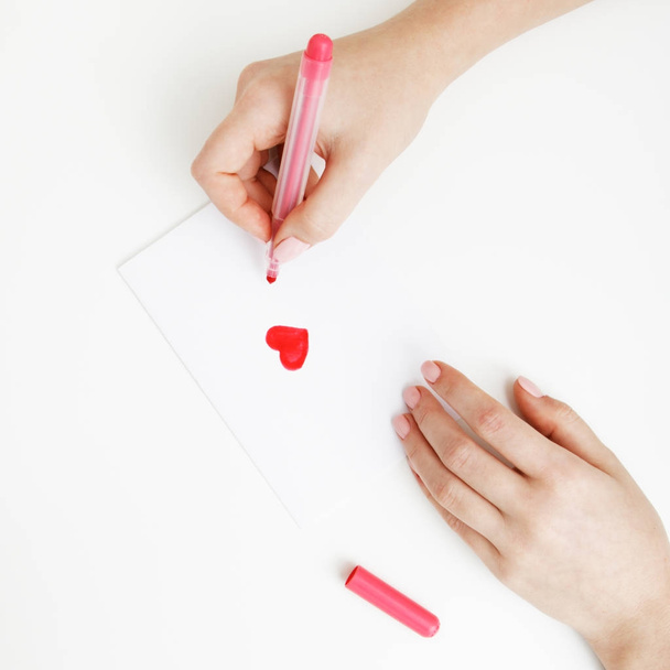 Flat lay. Top view. Hand of girl writing love letter on Saint Valentines Day. Handmade postcard with red heart shaped figure. Woman write Love on postcard for 14 February holiday celebration - Foto, Bild