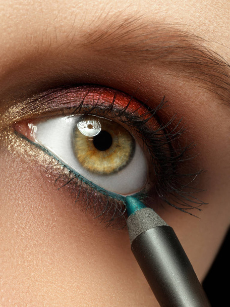Make-up met zwarte eyeliner close-up. Visagist eyeliner potlood toe te passen op een model met groene ogen - Foto, afbeelding