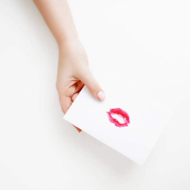 Flat lay. Top view. Hand of girl writing love letter on Saint Valentines Day. Handmade postcard with red lips shaped figure. Woman draw kiss on postcard for 14 February holiday celebration - Zdjęcie, obraz
