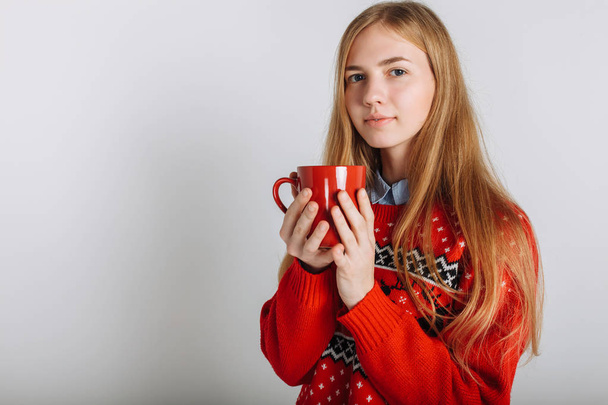Girl in a Christmas or new year sweater in the Studio holding a Cup of flavored coffee. Isolated place for text Christmas mood. - Foto, Imagem