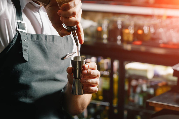 Мужские руки бармена крупным планом, делает коктейль на барной стойке, стаканы со льдом
. - Фото, изображение