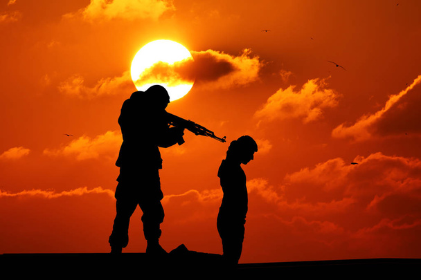 Silhouette of man with rifle pointed at victims back - Photo, Image